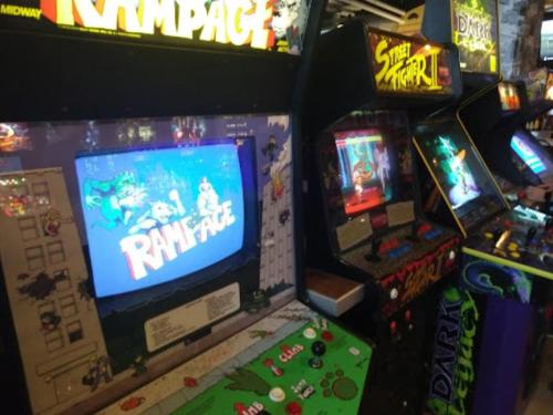 A retro arcade featuring "Rampage" and "Street Fighter" machines with colorful screens and classic controls.