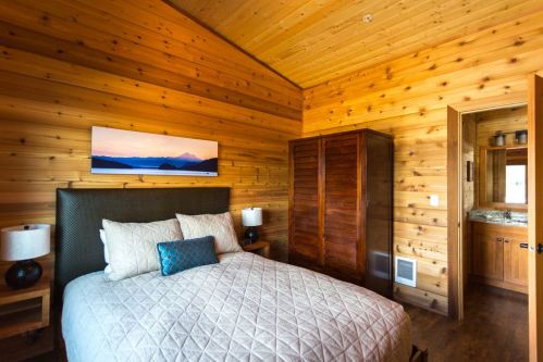 Cozy wooden bedroom with a queen bed, two lamps, a wardrobe, and a scenic painting on the wall.