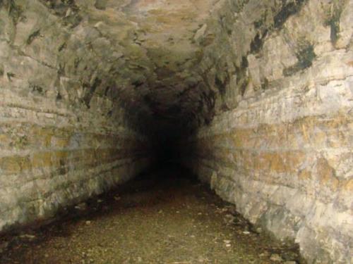 A dark, empty tunnel with rough stone walls and a gravel floor, extending into the distance.