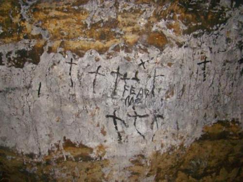 Graffiti on a rocky wall featuring multiple crosses and the words "FEAR ME."