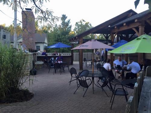 Outdoor patio with tables and umbrellas, people socializing, and a grill area in a relaxed setting.