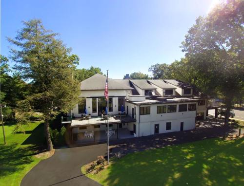 A large, modern building with a balcony, surrounded by trees and a well-maintained lawn on a sunny day.