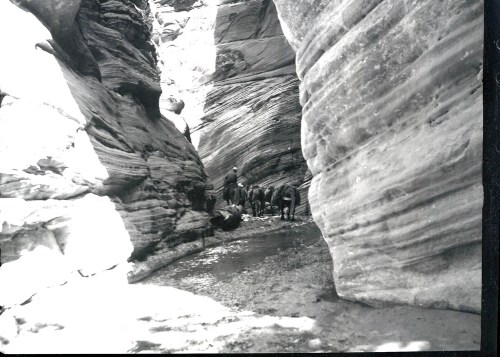 Black and white photo of a narrow canyon with people exploring the rocky terrain.