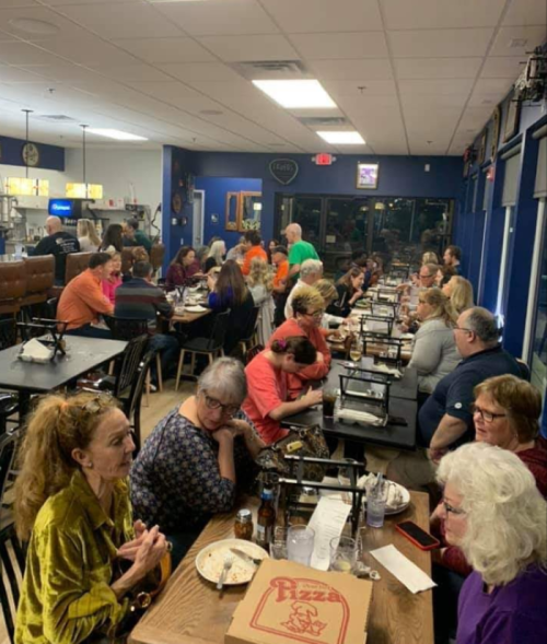 A lively restaurant scene with a large group of people dining and socializing at tables, enjoying food and drinks.