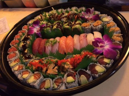 A beautifully arranged sushi platter featuring various rolls, sashimi, and garnished with flowers and greenery.