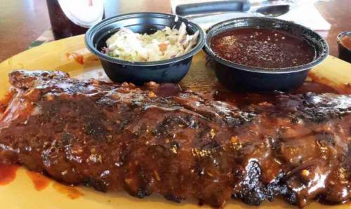 A plate of barbecue ribs glazed with sauce, accompanied by coleslaw and a small bowl of barbecue sauce.
