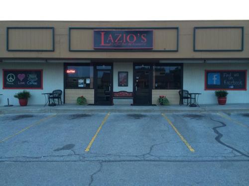Exterior of Lazio's Coffee Bar & Sweets, featuring a sign, potted plants, and outdoor seating in a parking lot.