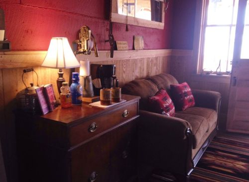 Cozy interior with a brown sofa, lamp, coffee maker, and wooden decor against a red wall. Warm and inviting atmosphere.