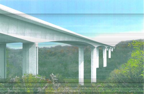 A modern bridge spans a valley, supported by tall white pillars against a backdrop of trees and a clear blue sky.