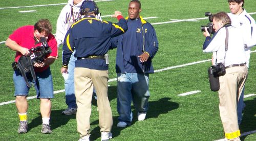 A group of people on a football field, with one man being interviewed and others filming and taking photos.