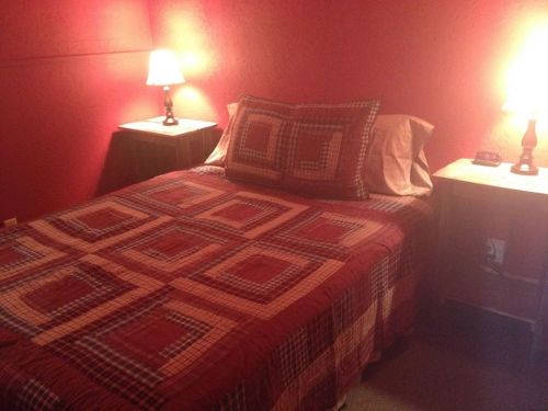 Cozy bedroom with a red wall, a patterned quilt on a bed, and two bedside lamps illuminating the space.