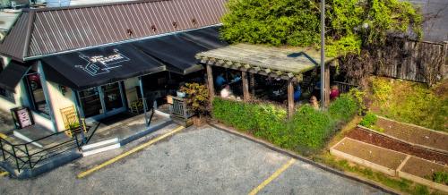 Aerial view of a restaurant with a patio, surrounded by greenery and garden beds, in a parking lot.