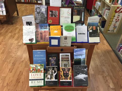 A wooden display featuring various books, including poetry and literature, arranged neatly in a bookstore.