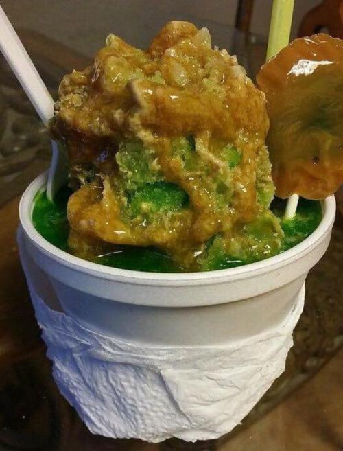 A cup of vibrant green shaved ice topped with a thick layer of caramel and a slice of fruit.