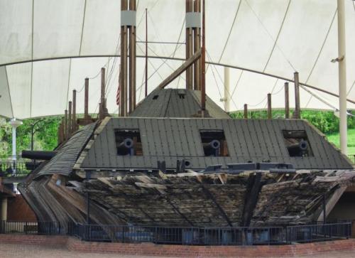 A historic shipwreck displayed under a large canopy, showcasing its weathered wooden structure and cannons.