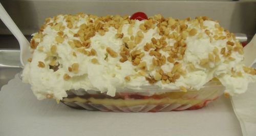 A dessert dish topped with whipped cream, chopped nuts, and a cherry, layered with fruit and cream.