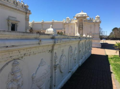A white ornate building with intricate designs, surrounded by a clear blue sky and a paved pathway.