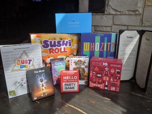 A collection of board games and a menu displayed on a table, featuring titles like "Sushi Roll" and "Just One."