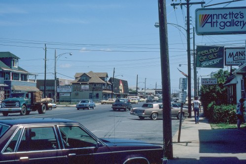 A busy street scene featuring shops, cars, and a sign for Annette's Art Gallery on a sunny day.