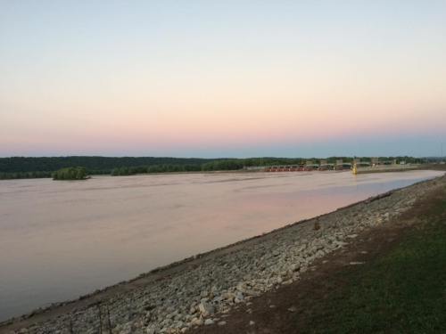 A calm river at dusk, with a soft gradient sky and lush greenery along the shore.