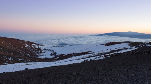 A serene landscape of snow-capped mountains above a sea of clouds at sunrise, with soft pastel colors in the sky.