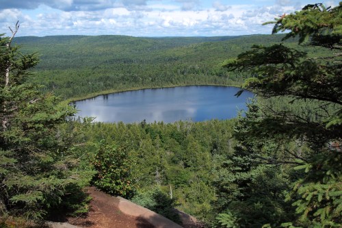 A serene view of a circular lake surrounded by lush green forests under a partly cloudy sky.