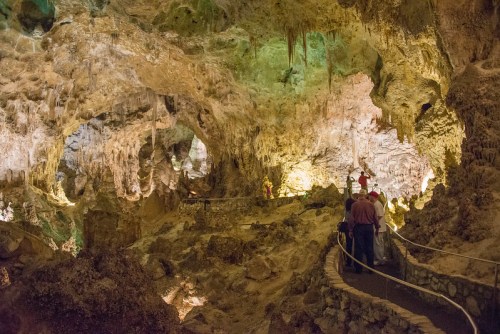 A dimly lit cave with colorful rock formations and visitors exploring along a winding path.
