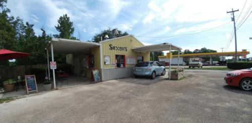 A small, yellow restaurant with a covered patio, parked cars, and a gas station in the background under a blue sky.