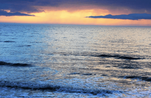 A serene ocean view at sunset, with waves gently lapping against the shore and a colorful sky in the background.