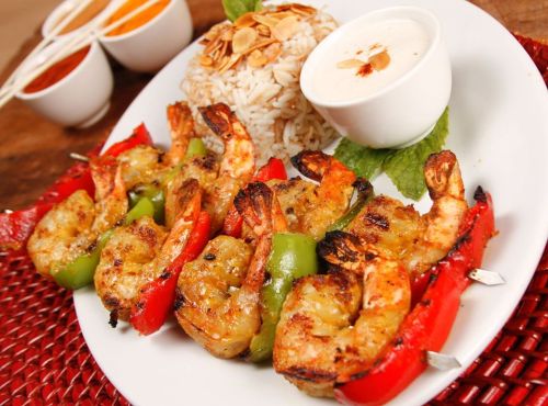 Grilled shrimp skewers with bell peppers, served with rice and dipping sauces on a white plate.