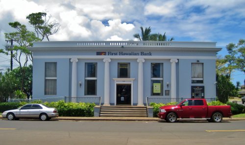Exterior of First Hawaiian Bank building, featuring columns and two parked cars in front under a blue sky.