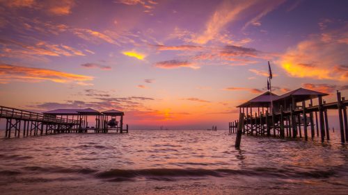 Sunset over a calm bay, with wooden piers and colorful clouds reflecting on the water's surface.