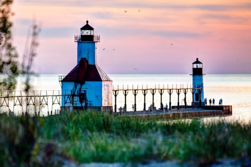 A scenic view of a lighthouse pier at sunset, with people walking along the dock and calm waters in the background.