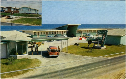 A vintage postcard of a seaside motel with cars, umbrellas, and a view of the ocean in the background.