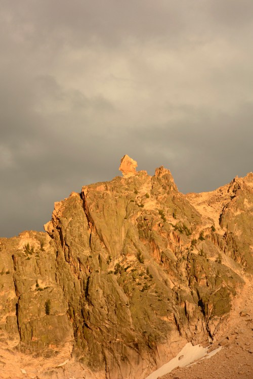 A rugged mountain peak illuminated by soft light under a cloudy sky, showcasing dramatic rock formations.