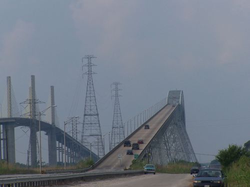 A highway bridge with vehicles crossing, flanked by power lines and under a cloudy sky.