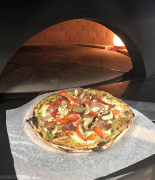 A freshly baked pizza with red peppers, mushrooms, and ham, placed in a wood-fired oven.
