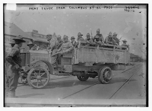 A historic army truck with soldiers seated in the back, parked on a railway track in El Paso.