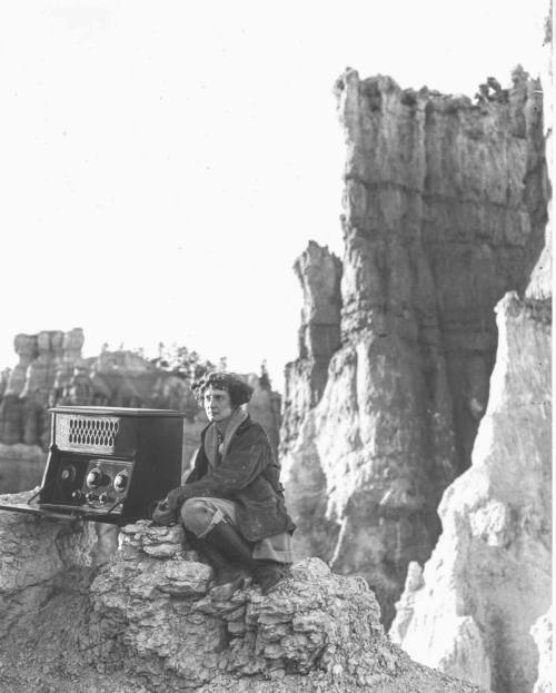 A person in a coat sits on a rock near a vintage radio, surrounded by towering rock formations.