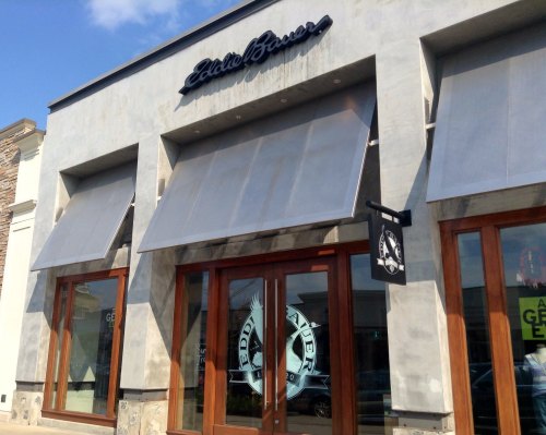 Exterior of a store named "Eddie Bauer," featuring large windows and awnings under a clear blue sky.
