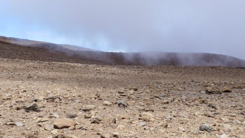 A barren landscape with rocky terrain and low clouds, suggesting a volcanic or arid environment.