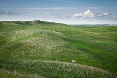Lush green hills under a blue sky with scattered clouds, creating a serene landscape.