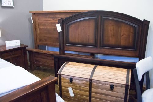 A display of wooden furniture including a bed frame, headboard, and a storage chest in a showroom setting.