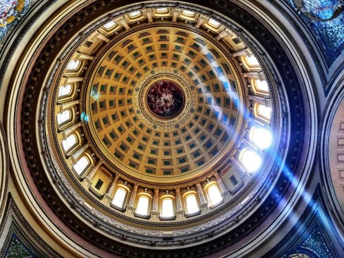A view looking up at a beautifully decorated dome with intricate patterns and sunlight streaming through the windows.