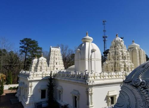 A white temple with intricate architecture, surrounded by trees under a clear blue sky.