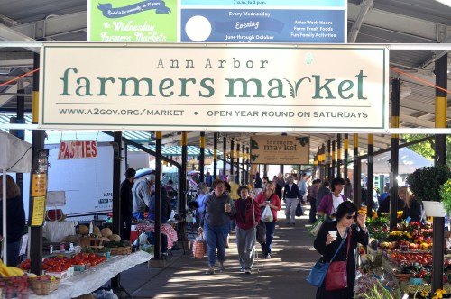 A bustling farmers market in Ann Arbor, with vendors and shoppers among colorful produce and goods.
