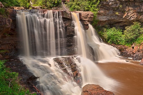 A serene waterfall cascades over rocky cliffs, surrounded by lush greenery and a tranquil river below.