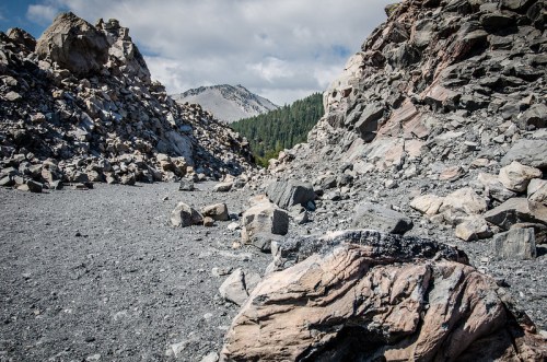 Rocky landscape with large boulders and a mountain in the background under a partly cloudy sky.