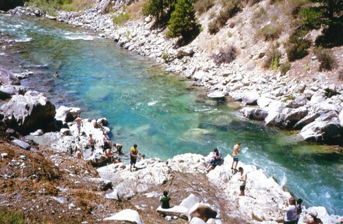 A scenic river with clear blue water, surrounded by rocky banks and people enjoying the outdoors.