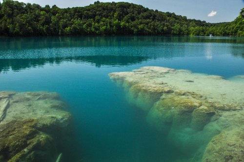 Clear turquoise water reflects a lush green landscape, with rocky formations visible beneath the surface.